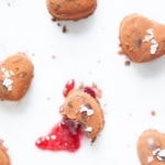 Vegan chocolate raspberry truffles on white background with jam spilling out of one truffle.