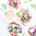 Roasted squash tacos on a white background with a small white bowl of chipotle tahini crema.