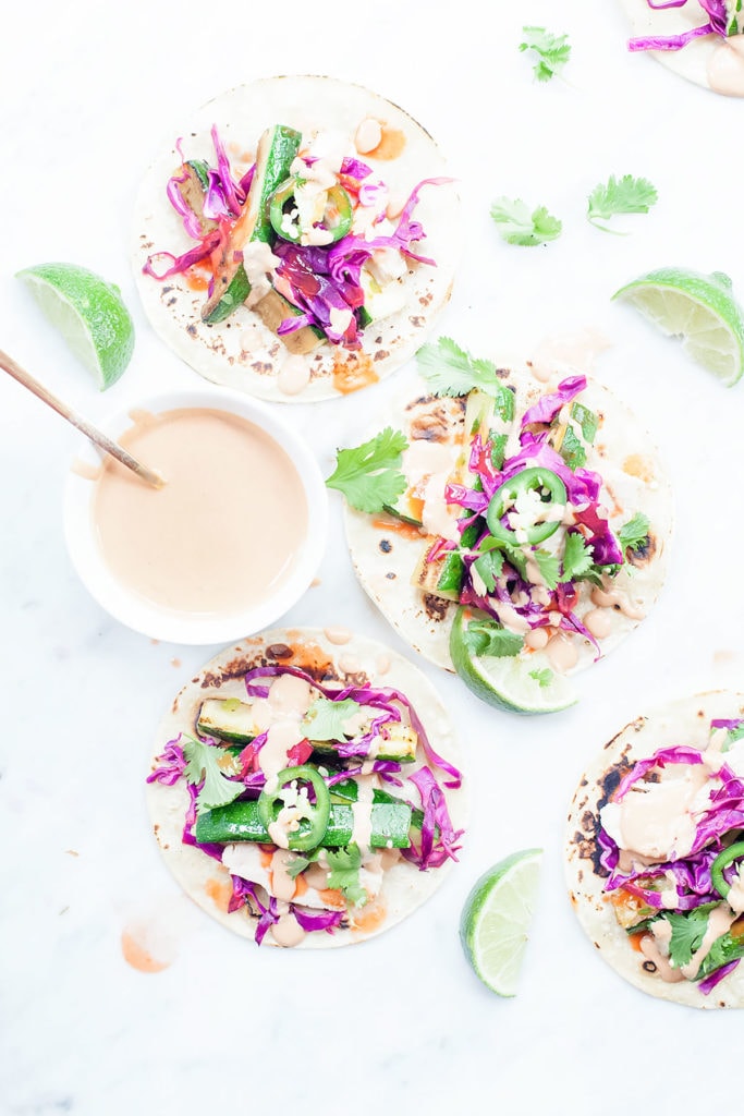 Roasted squash tacos on a white background with a small white bowl of chipotle tahini crema.