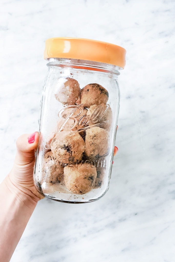 Seed cycling brownie bites in a glass jar being held.