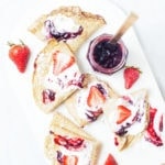 Gluten-free crepes with coconut whipped cream, strawberries, and jam on a white platter.