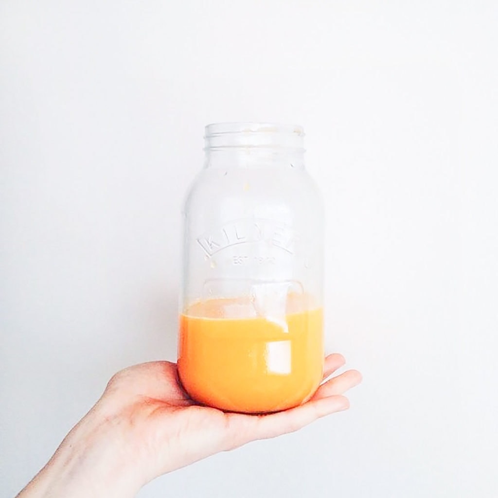 Orange smoothie in a mason jar being held by a hand.