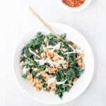Tuscan beans with spicy sausage and kale in a white bowl with red pepper flakes.