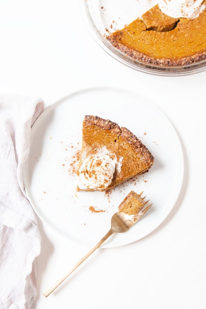 Gluten-free, dairy-free pumpkin pie slice on a white plate with a dollop of coconut whipped cream.