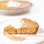 Gluten-free, dairy-free pumpkin pie slice on a white plate with a dollop of coconut whipped cream.