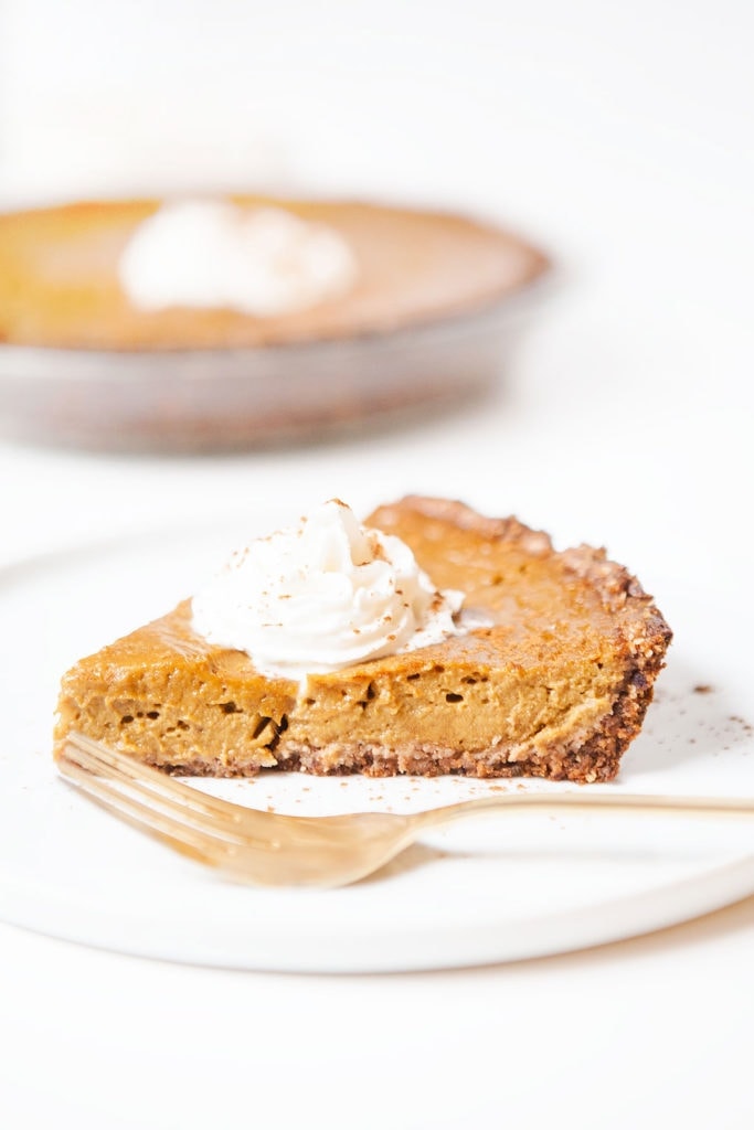 Gluten-free, dairy-free pumpkin pie slice on a white plate with a dollop of coconut whipped cream.