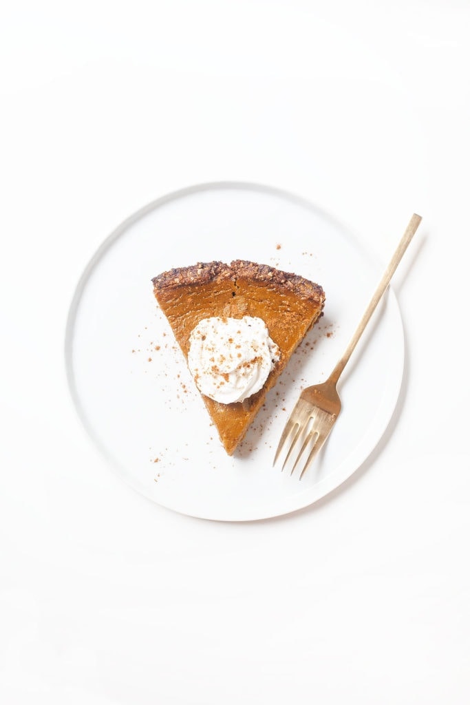 Gluten-free, dairy-free pumpkin pie slice on a white plate with a dollop of coconut whipped cream.