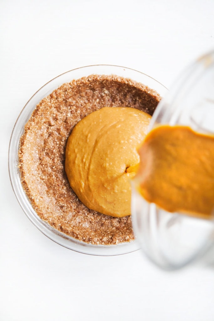 Gluten-free, dairy-free pumpkin pie filling being poured into a pecan oat pie crust.