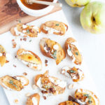 Pear and goat cheese crostini on a white platter with a small bowl of honey.