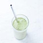 Green smoothie in a glass with a metal straw.