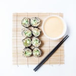 Avocado cucumber vegan sushi rolls on a bamboo sheet with a bowl of tahini miso sauce.