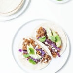 Lentil tacos on a white plate with avocado and limes.