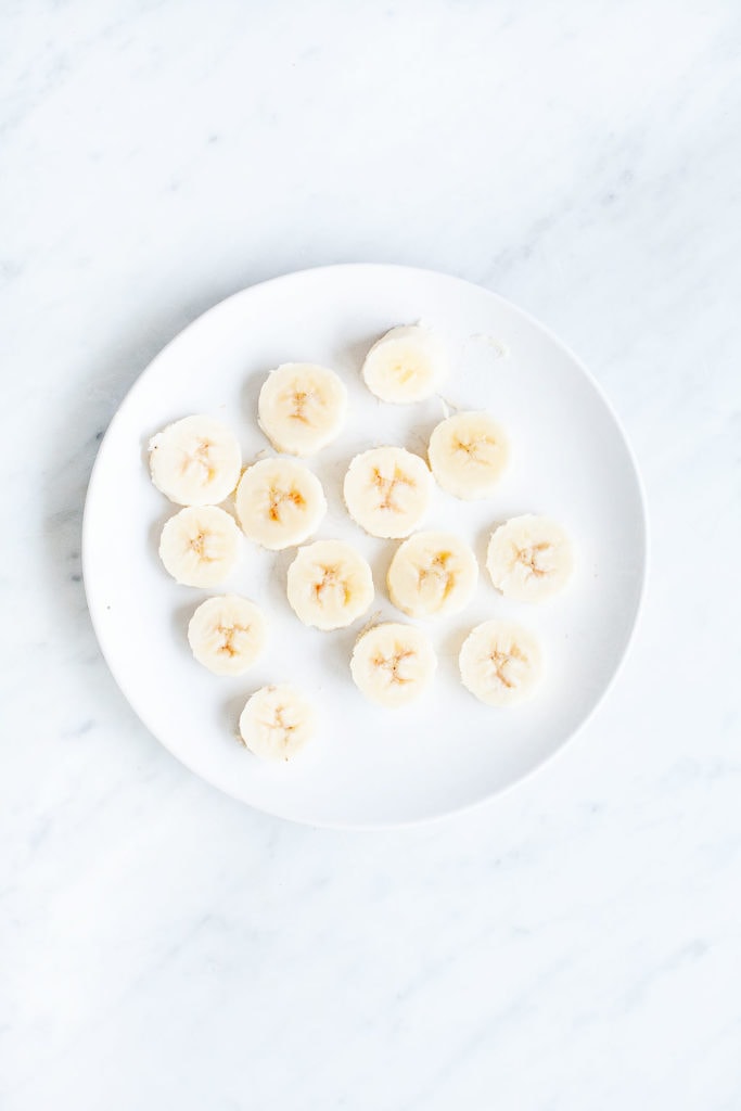 Bananas cut into coins on a white plate.