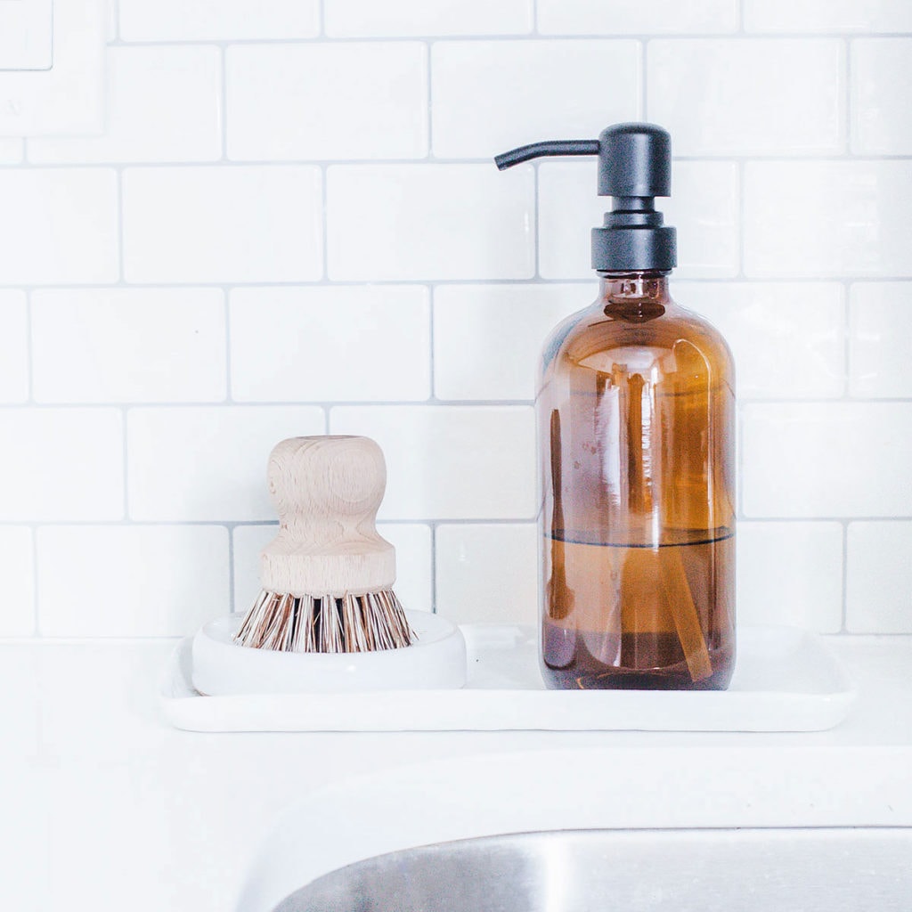 Dish brush and amber glass soap dispenser next to a sink.