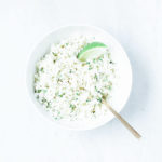 Coconut cauliflower rice with cilantro and a slice of lime in a white bowl.