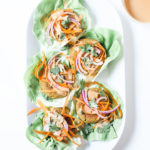 Peanut edamame burgers wrapped in lettuce on a white platter from above with a small bowl of coconut peanut sauce.