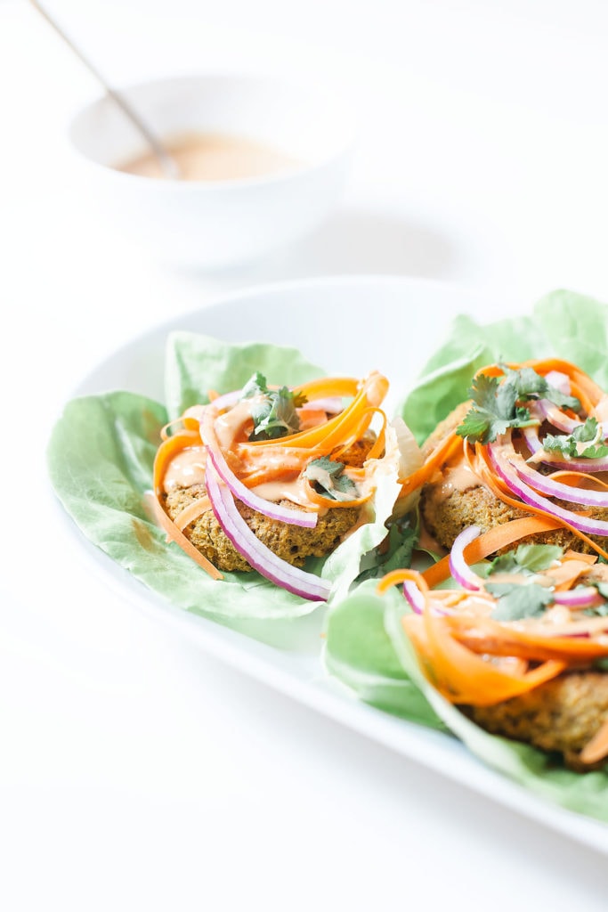 Peanut edamame burgers wrapped in lettuce on a white platter from the side.