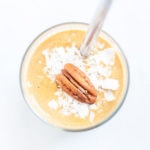 Pumpkin pie smoothie in a glass with a straw from above with a pecan on top.