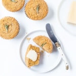 Gluten-free rosemary cornbread muffins on a white surface with a pat of butter.
