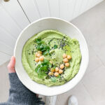 Avocado hummus in a white bowl being held by a hand.