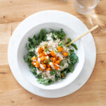 Baked buffalo tofu with kale and brown rice in a white bowl on a table.