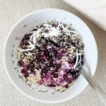 Overnight oats with blueberries and coconut in a white bowl with fabric background.